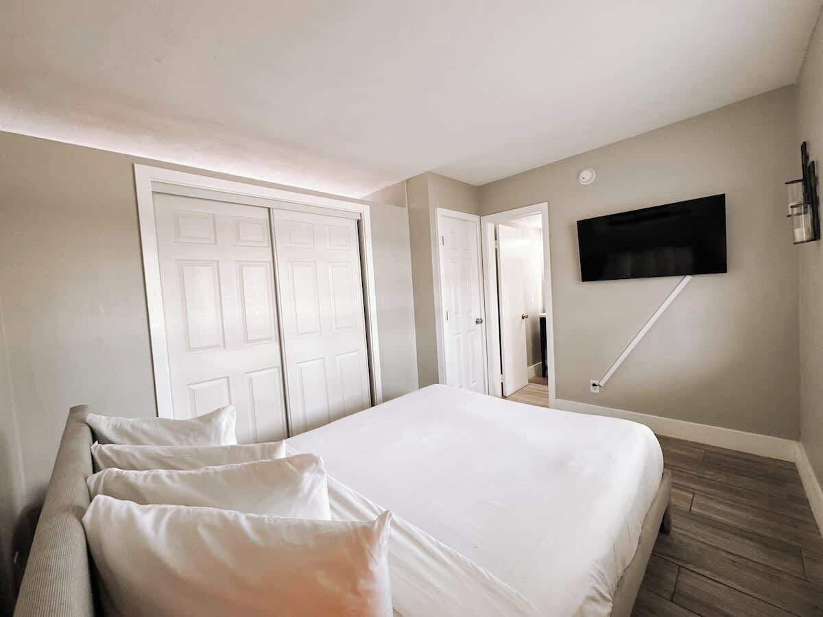 Een slaapkamer met een groot bed, een flatscreen televisie aan de muur en een deur naar een andere kamer.