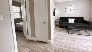Una habitación con una puerta cerrada, un sofá oscuro, una mesa de centro y un reloj de pared.