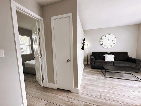 A room with a closed door, a dark sofa, a coffee table, and a wall clock.