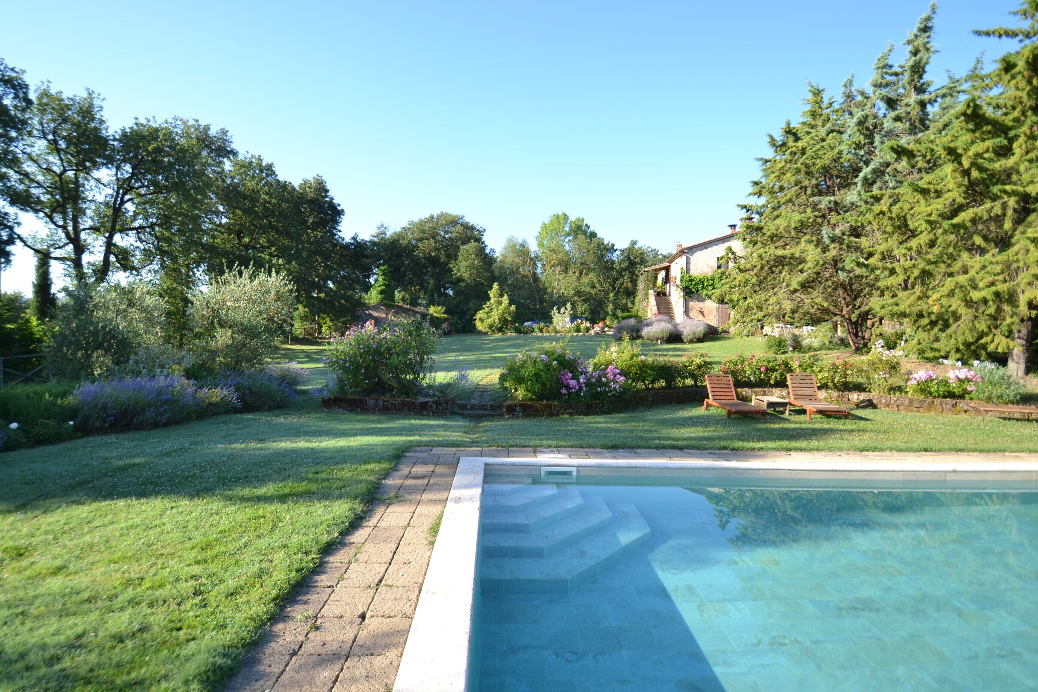 Ein Swimmingpool mit Blick auf den umliegenden Garten und ein Steinhaus im Hintergrund.