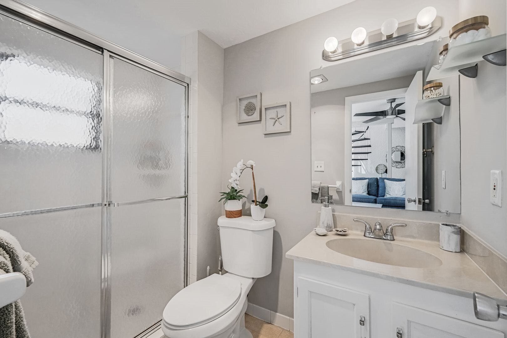 Et badeværelse med toilet, håndvask og bruser. Der er lys over spejlet og en bøjle til håndklæder.