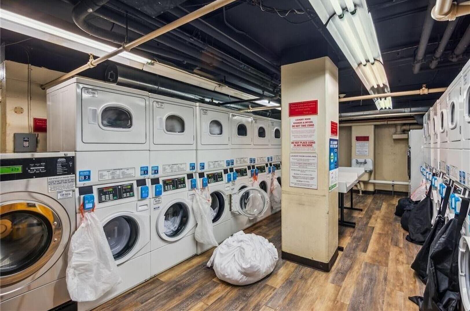 A laundry facility with multiple washing machines, a wooden floor, and a sign instructing not to place coins in machines.