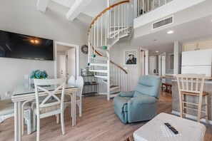 Un vaste espace de vie agrémenté d’un escalier en colimaçon, d’une table à manger avec des chaises, d’un canapé et d’un coin cuisine à l’arrière-plan.