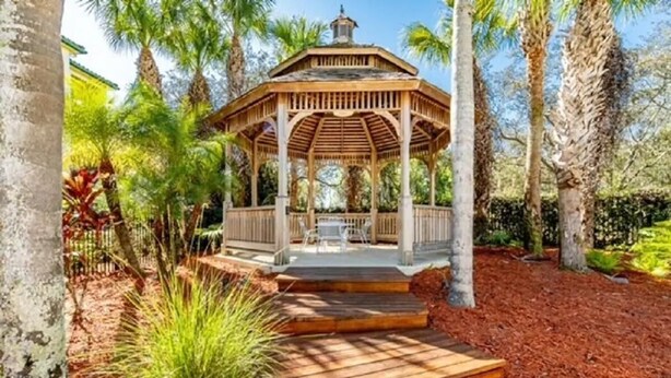 A wooden gazebo with a covered seating area, surrounded by palm trees and a mulched ground. - Cozy Condo minutes away from Disney (Kissimmee)