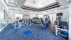 A spacious gym with various exercise equipment, including treadmills and weight machines, and a blue carpeted floor. - Cozy Condo minutes away from Disney (Kissimmee)