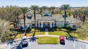 A large, multi-story building with a symmetrical facade, a central entrance, and a parking area with two cars. - Cozy Condo minutes away from Disney (Kissimmee)