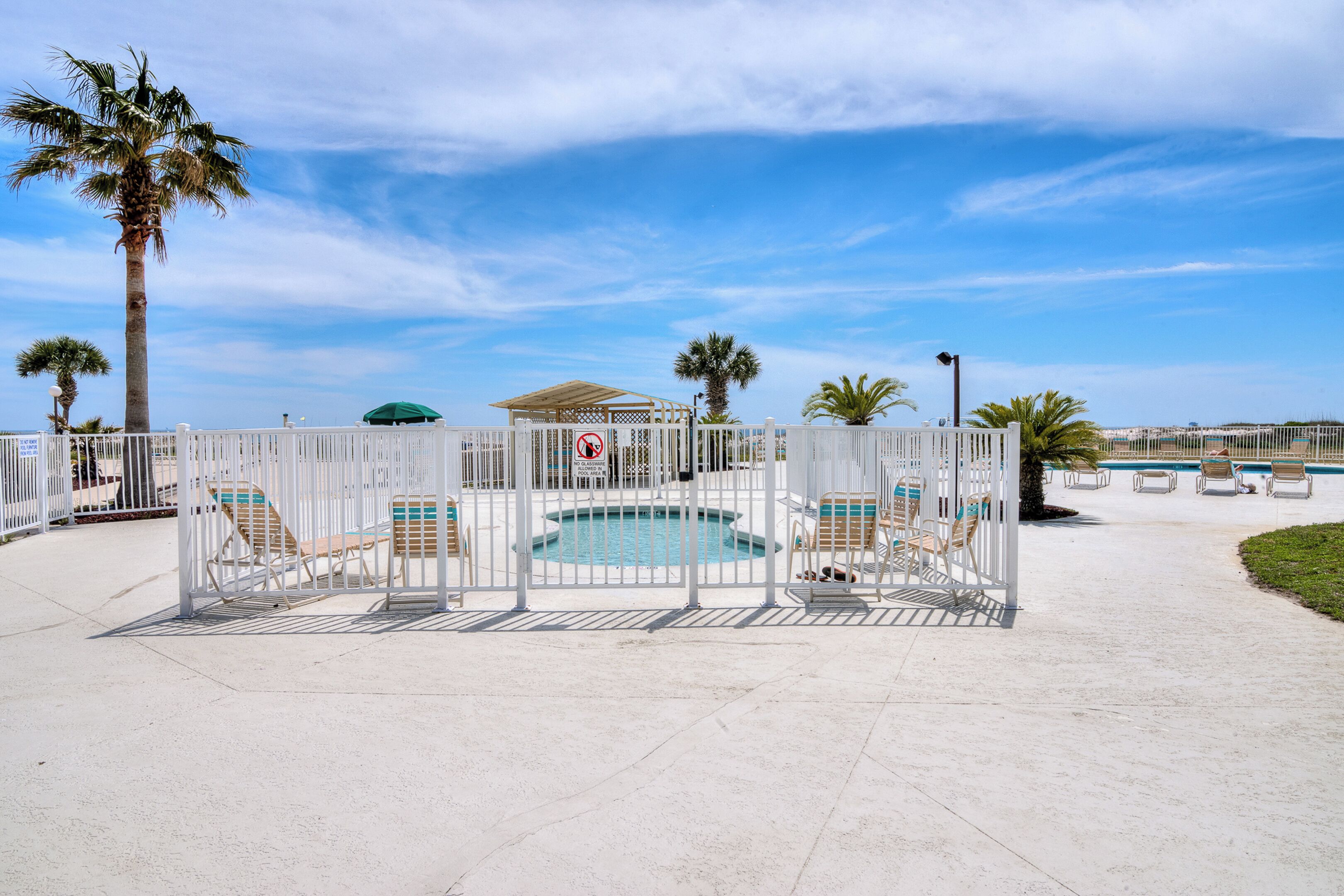 A fenced pool area with lounge chairs and a pool.