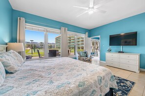 Une chambre avec un grand lit, une télévision, une commode et une vue sur un immeuble et un parc.