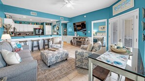 A modern living room with a sofa, ottoman, and a glass coffee table. - Gulf Shores Plantation-Dunes 5005 (Gulf Shores)