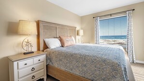 A bedroom with a bed, nightstands, and a view of the beach. - Gulf Shores Plantation-Palms 6512 (Gulf Shores)