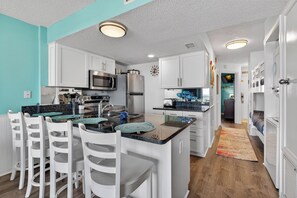 A modern kitchen with white cabinetry, stainless steel appliances, and a teal accent wall.