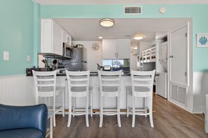 Una cocina con armarios blancos, un refrigerador de acero inoxidable y una barra con sillas blancas.