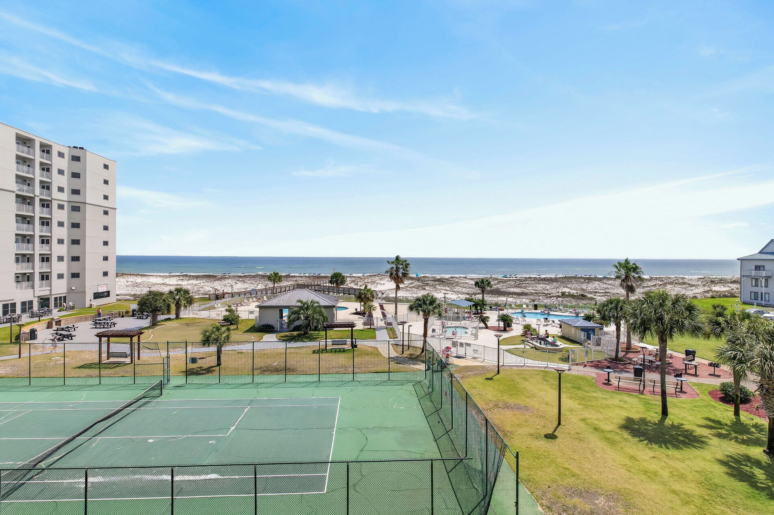 A tennis court, a pool, and a beach view.