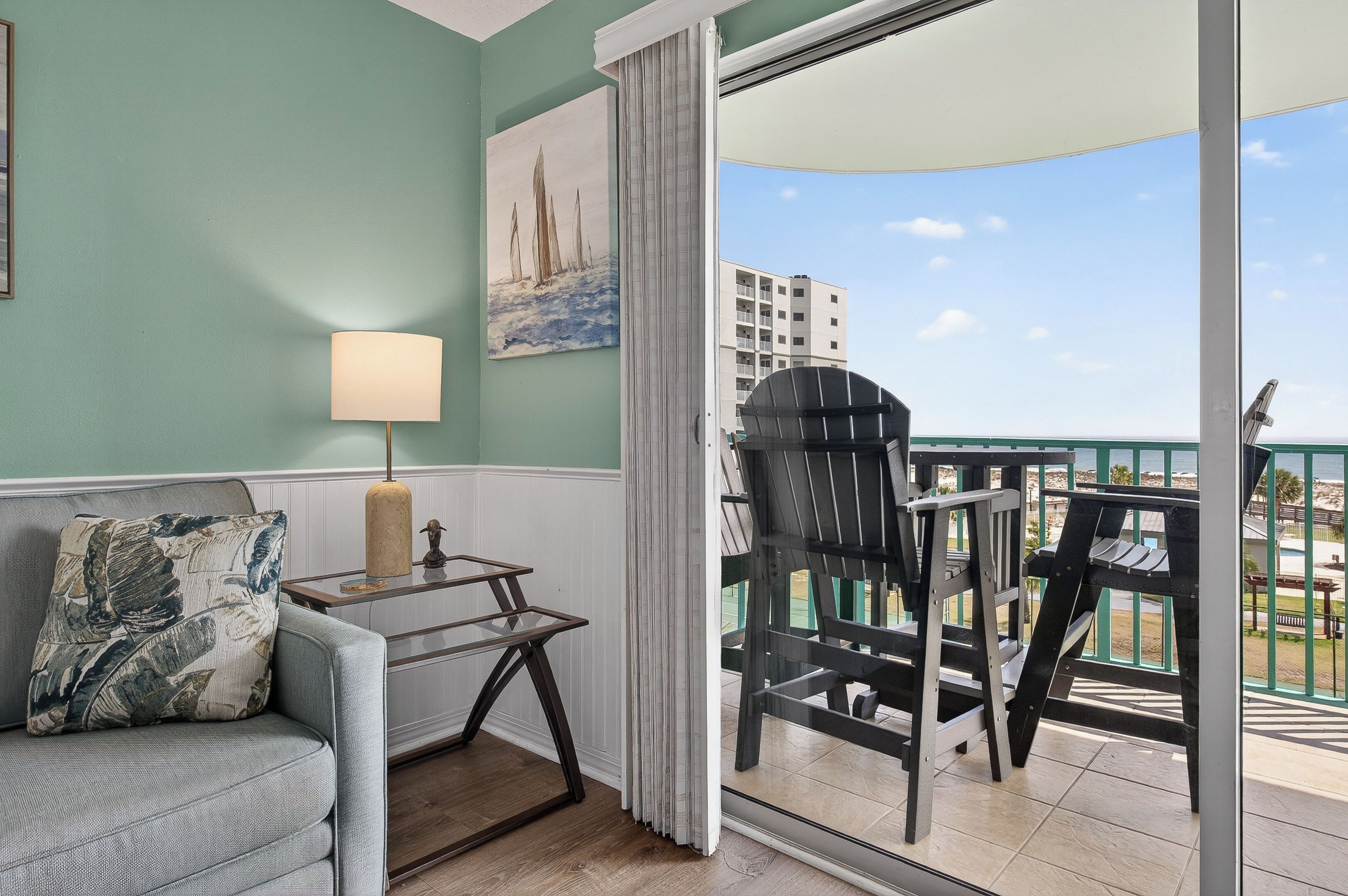 Ein Balkon mit Blick auf das Meer und Gebäude, eine Sitzecke mit Kissen, ein Tisch mit Lampe sowie ein Gemälde an der Wand.
