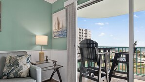 Een balkon met uitzicht op zee en gebouwen, een bank met een kussen, een tafel met een lamp, en een schilderij aan de muur.