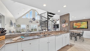 A spacious kitchen with a granite countertop, white cabinets, and a black spiral staircase.