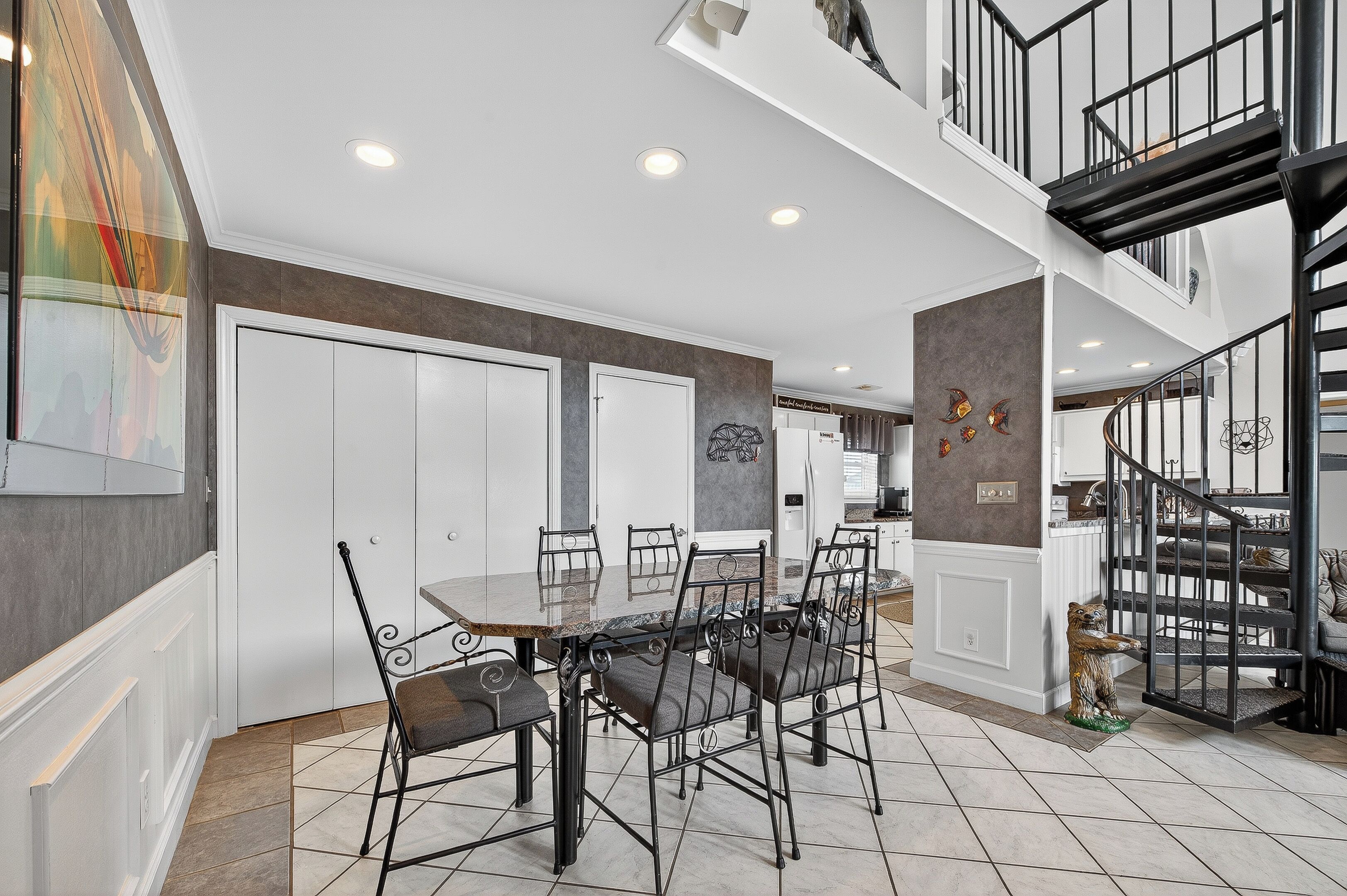 Un espace repas avec une grande table et des chaises, un escalier et une vue sur la cuisine.