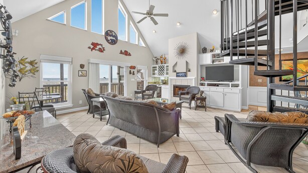 A spacious living area with a high ceiling, large windows, a dining area, and a kitchen.