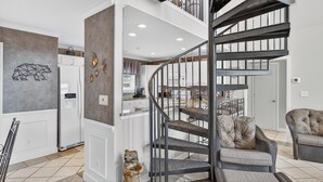 A modern kitchen with a built-in refrigerator, a dining area with wicker furniture, and a spiral staircase.