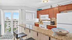 Una cocina moderna con encimeras de granito, gabinetes de madera, microondas, estufa y refrigerador.