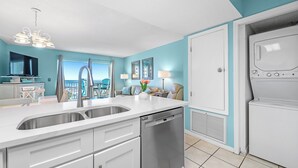 A modern kitchen with a dishwasher, a sink, and a microwave. There is a view of the ocean through large windows. - Gulf Shores Plantation-Palms 6406 (Gulf Shores)
