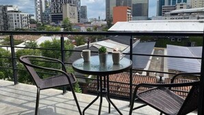 Ein Balkon mit zwei Korbstühlen und einem kleinen Tisch, mit Blick auf eine Stadtlandschaft und moderne Gebäude.