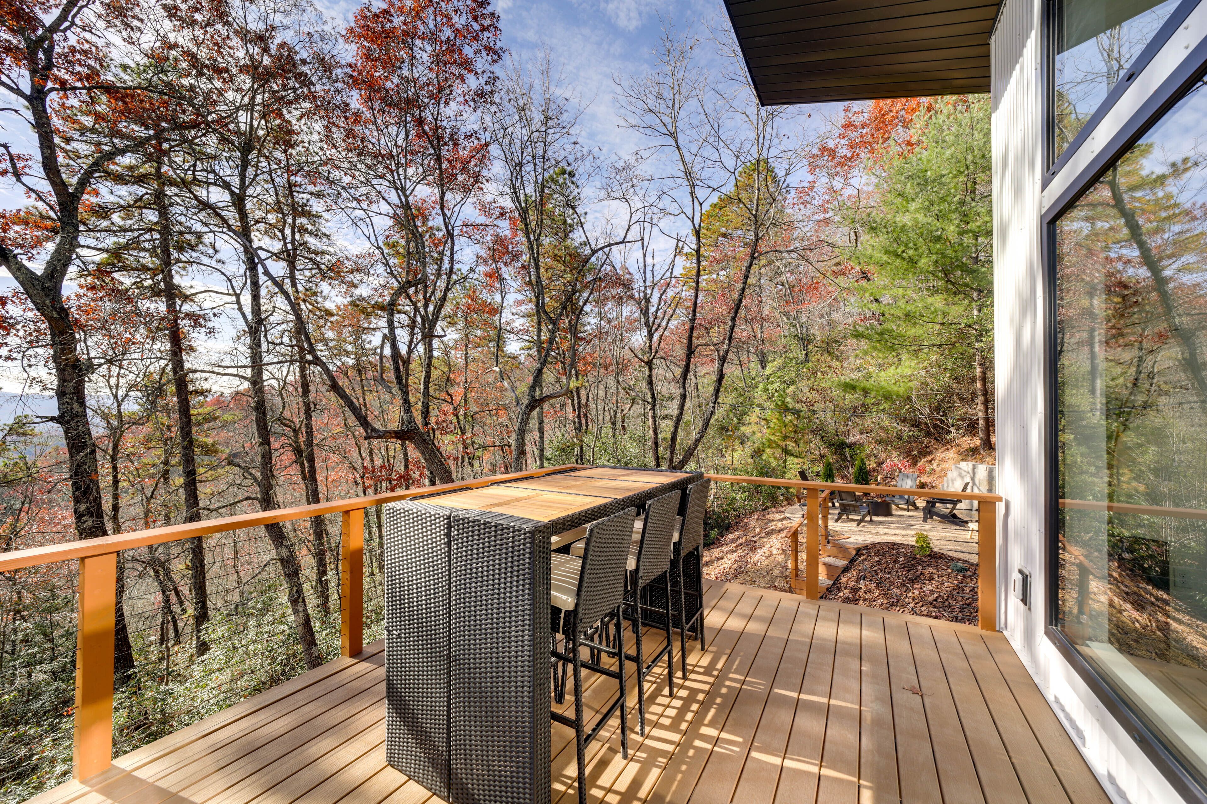 A wooden deck with a table and chairs, overlooking a forested area with autumn foliage.