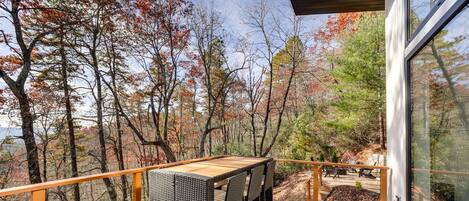 A wooden deck with a table and chairs, overlooking a forested area with autumn foliage.
