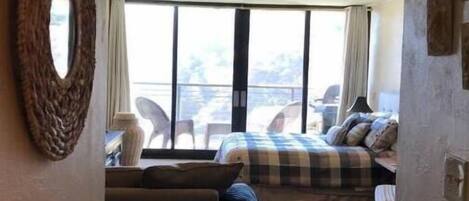 A hotel room with a large bed, a sofa, and a view of the outdoors through large windows.