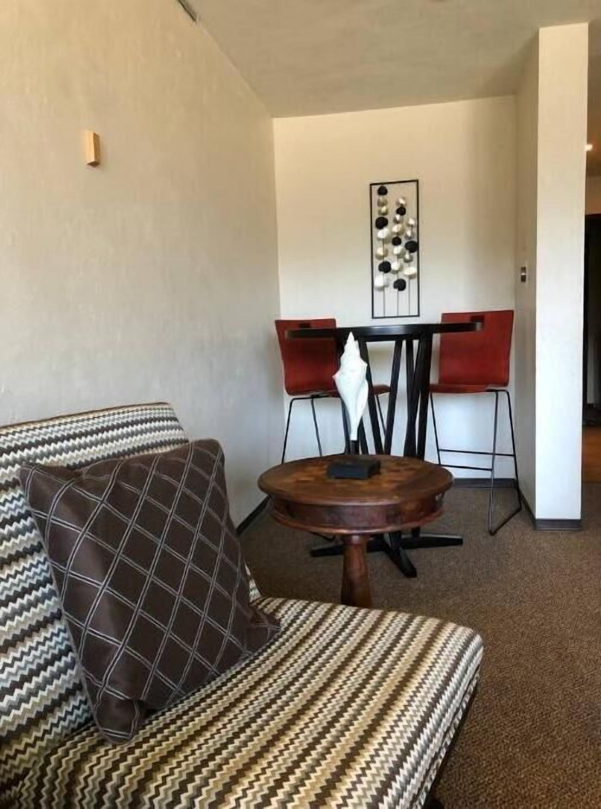 Una sala de estar con un sofá estampado, una mesita redonda y un comedor con sillas rojas y una mesa blanca.