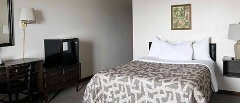 A hotel room with a bed, a desk with a TV, a dresser, and a painting on the wall.