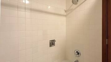 Une salle de bain avec des murs carrelés de carreaux blancs, une baignoire, une pomme de douche et un porte-serviettes.