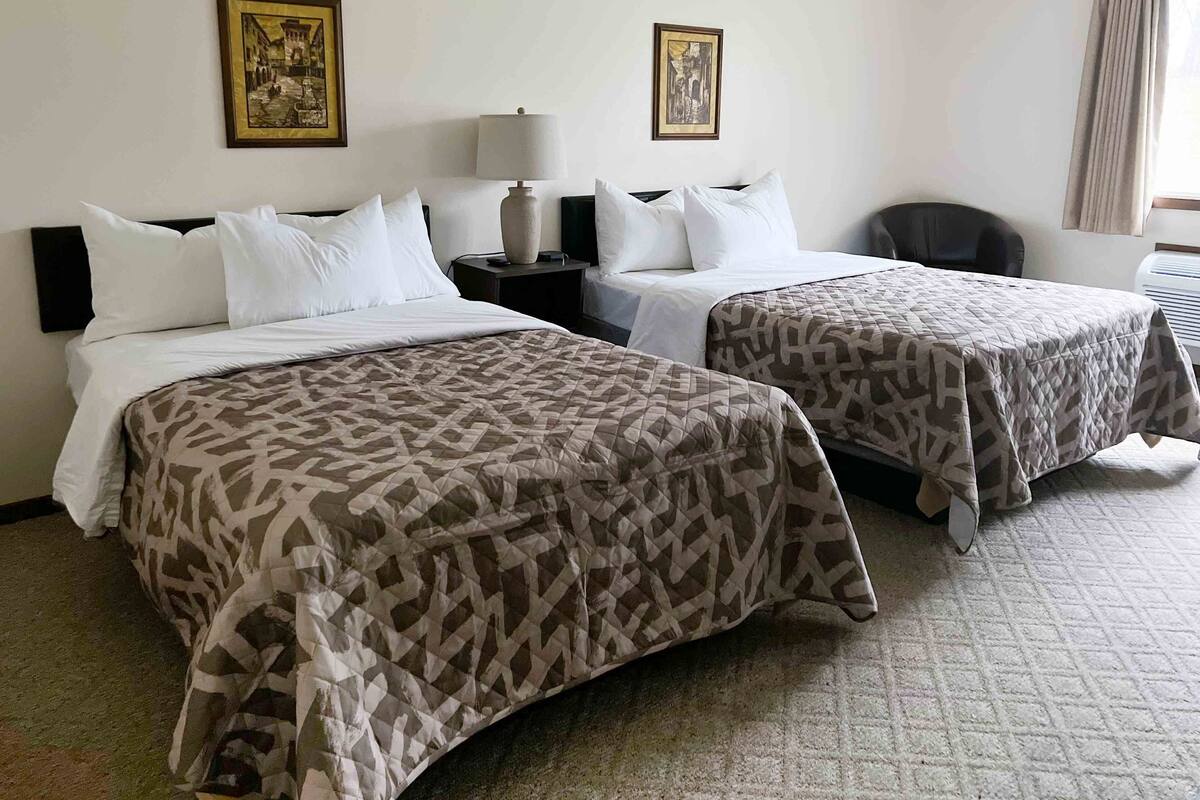 A hotel room with two beds, each with a patterned bedspread, a nightstand with a lamp, and two framed pictures on the wall.