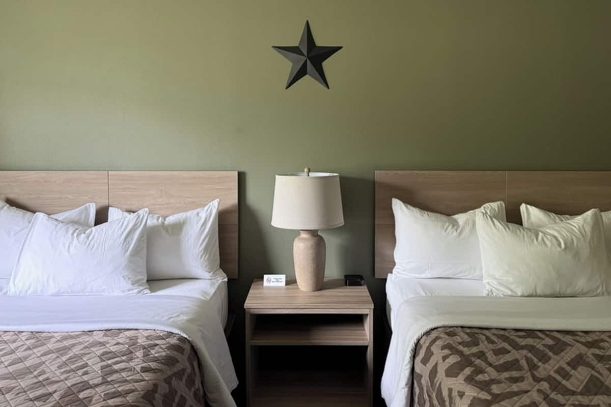 A hotel room with two beds, a nightstand with a lamp, and a wall-mounted star decoration.
