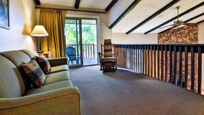Une pièce comprenant un canapé, une lampe, un fauteuil, un mur en pierre et un balcon avec une balustrade.
