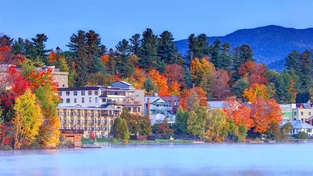 Une ville située au bord d’un lac, avec des immeubles à plusieurs étages, un quai et un feuillage automnal.