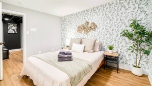 A bedroom with a bed, a nightstand, a wall-mounted decoration, and a potted plant.