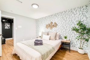 A bedroom with a bed, a nightstand, a wall-mounted decoration, and a potted plant.