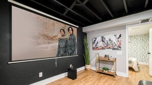 A room with a large projection screen, a wooden floor, a small plant, and a metal cart with items on it.