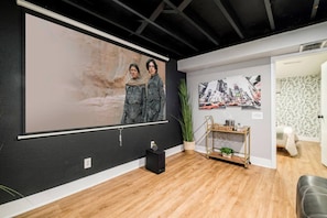 A room with a large projection screen, a wooden floor, a small plant, and a metal cart with items on it.