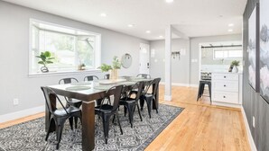 A modern kitchen with a dining area, featuring a large table, chairs, and a window with plants.