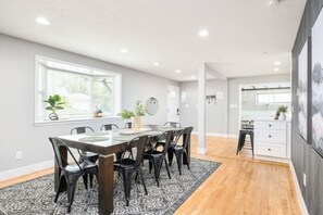 A modern kitchen with a dining area, featuring a large table, chairs, and a window with plants.