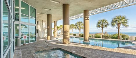 A pool area with a view of the ocean, surrounded by palm trees and a covered walkway.