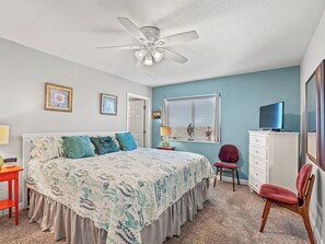 Une chambre à coucher avec un lit, un ventilateur de plafond, une télévision et une commode.