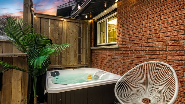 Un bain à remous avec une terrasse en bois et un mur en briques, une chaise blanche et une plante en pot.