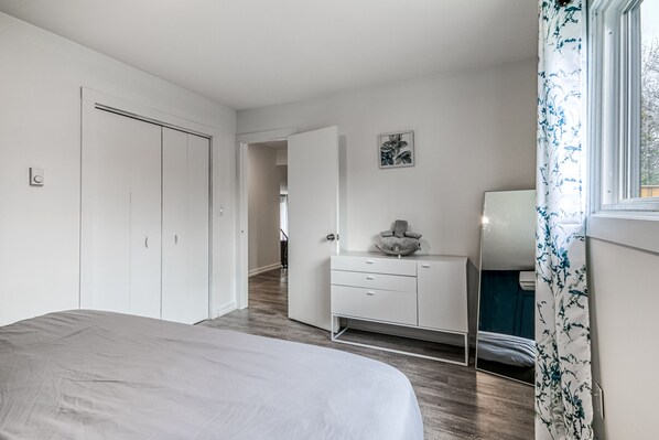 Une chambre à coucher comprenant un lit, une commode, un miroir et une porte donnant sur une autre pièce.