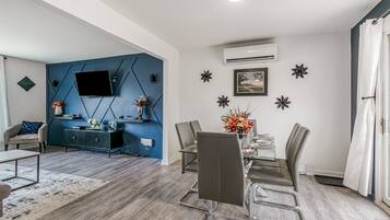 A modern living room with a blue accent wall, a mounted TV, a dining area with a table and chairs, and a decorative wall with star-shaped ornaments.