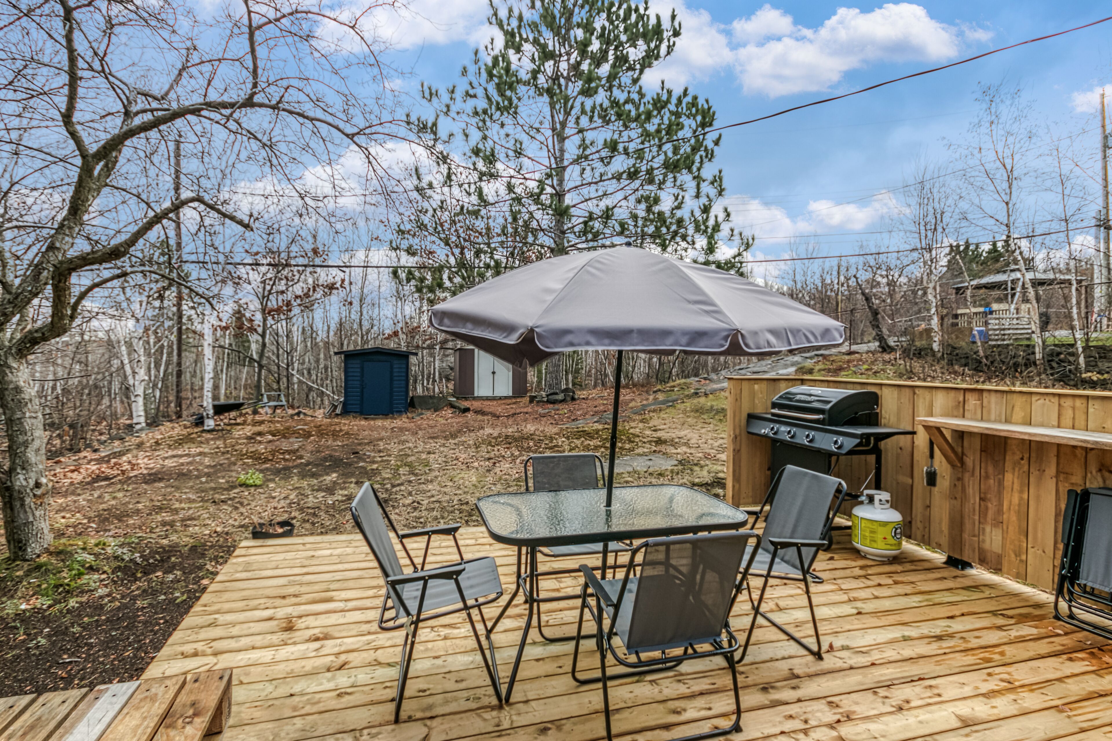 A wooden deck with a table and chairs, a grill, and an umbrella.