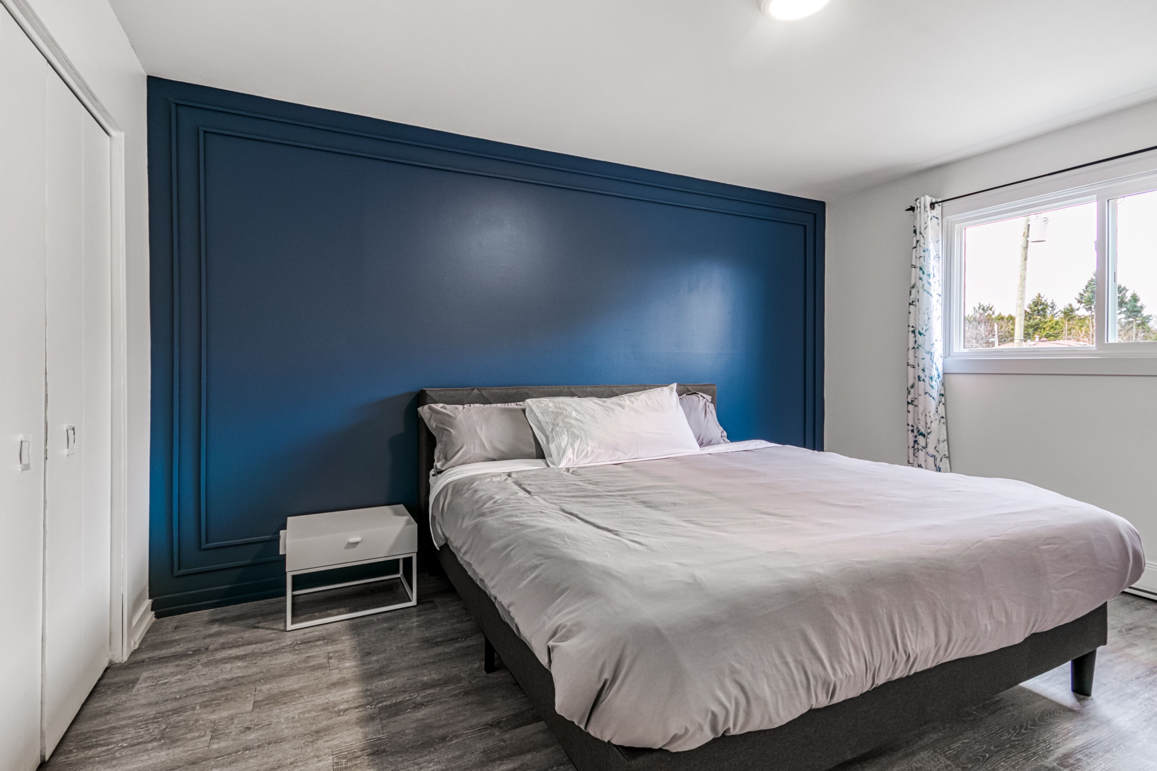 A bedroom with a bed, a nightstand, and a window with curtains.