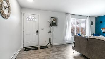 Ett modernt vardagsrum med en grå soffa, en vit dörr och ett stort fönster med gardiner.